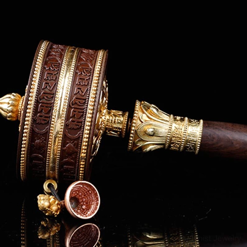 Horizontal low-angle view of prayer wheel featuring carved religious scriptures, gold hardware, and small hanging bell