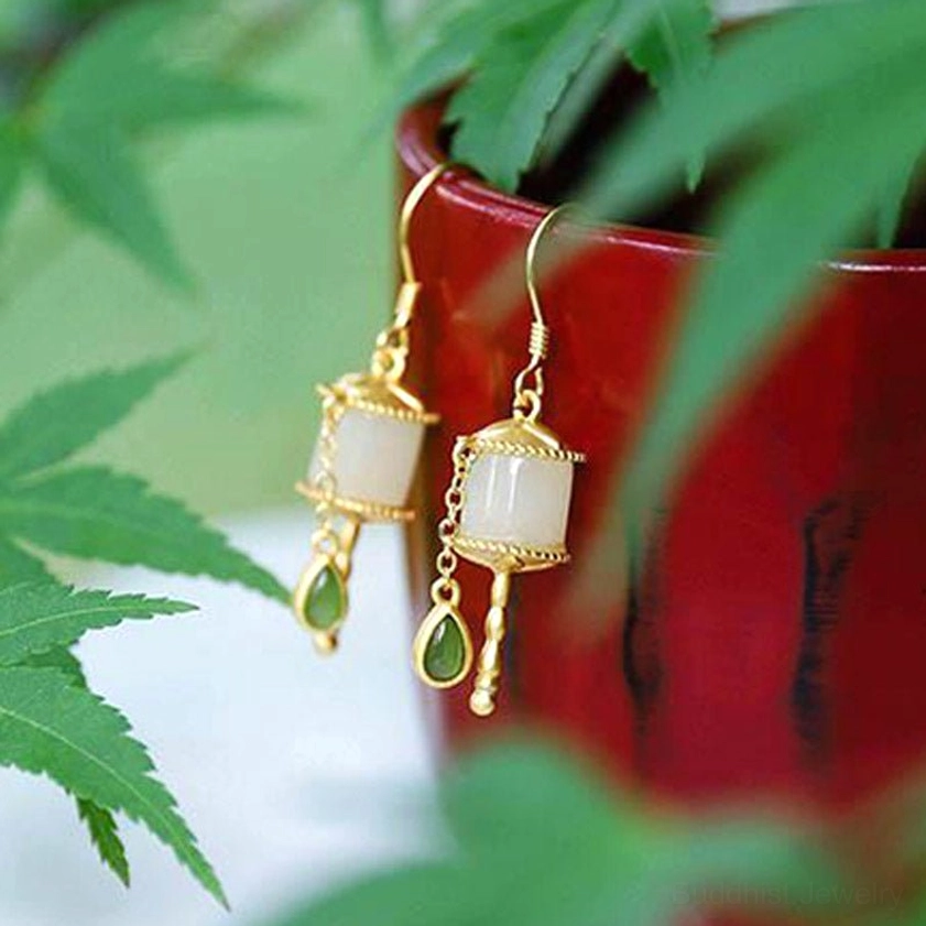 Buddhist jade prayer wheel dangle earrings in oblique angle view with red flower pot and maple leaves background, gold silver emerald green design