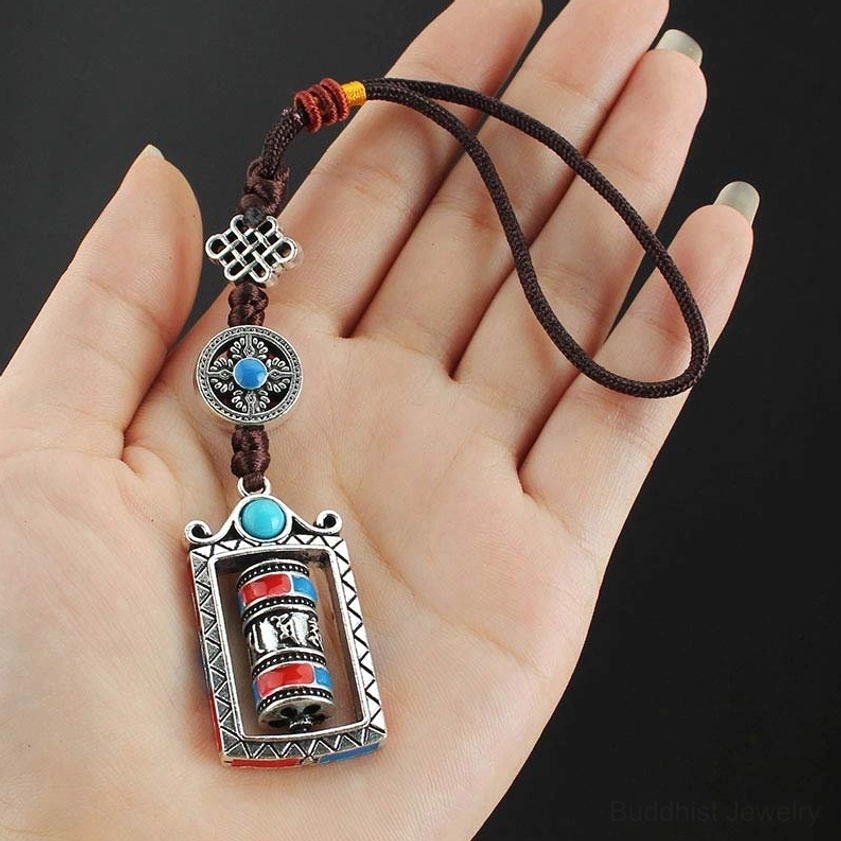 Prayer wheel keychain held in hand showing rotatable cylinder and adjustable brown lanyard