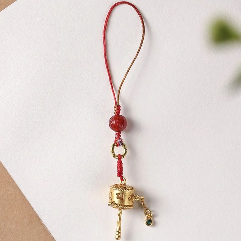 Single prayer wheel hanging lanyard with solid red braided strap and gold prayer wheel on white background