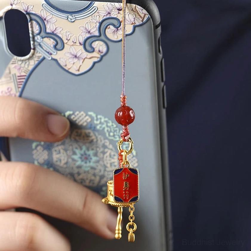 Buddhist prayer wheel phone charm attached to Chinese-style phone case showing red agate bead and gold ornament