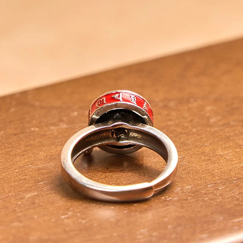 Bottom view of rotatable prayer wheel ring showing adjustable open copper band and rotating red enamel mechanism