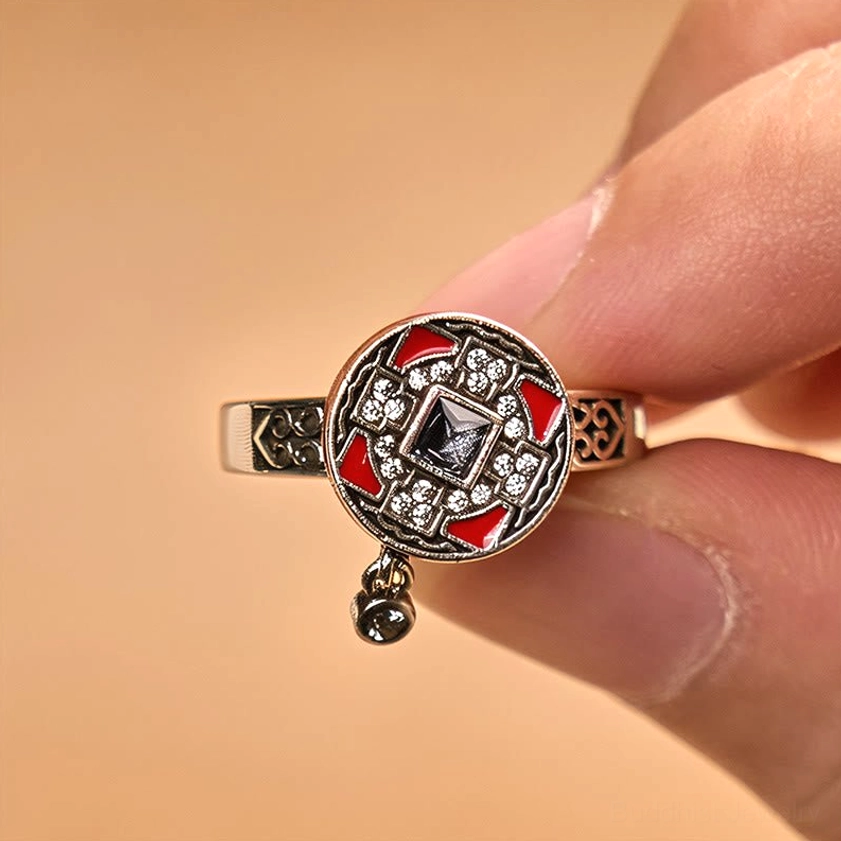 Copper Buddhist prayer wheel ring worn on fingertip, close-up detail showing dangling bell charm and engraved band