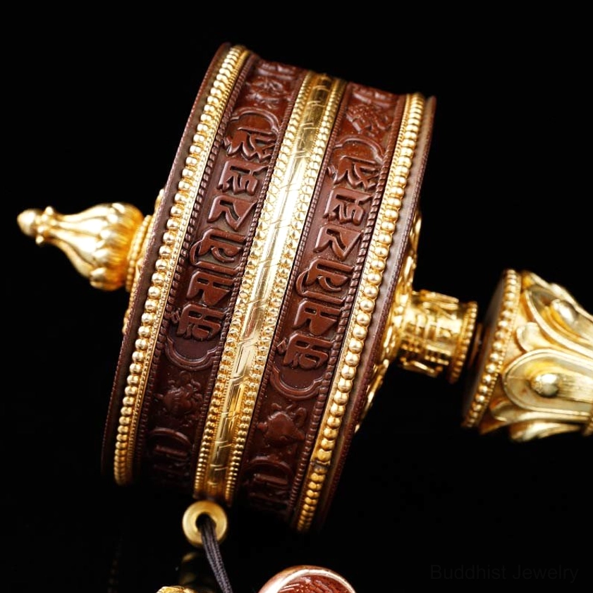 Side profile of meditation prayer wheel showing vertical Sanskrit carvings, gold central spindle, and hanging loop