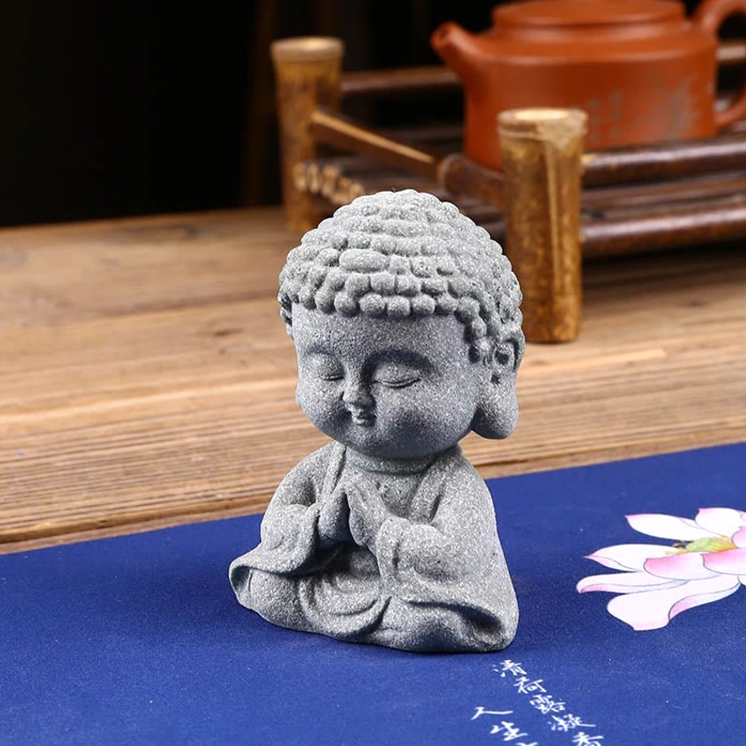 Praying Buddha ornament three-quarter side view placed on lotus pattern blue mat with tea set on wooden desk