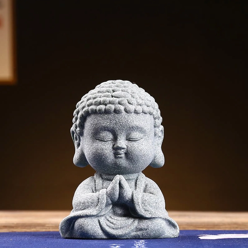 Close-up front view of praying Buddha statue with clasped hands and curly hair bun in natural sandstone finish
