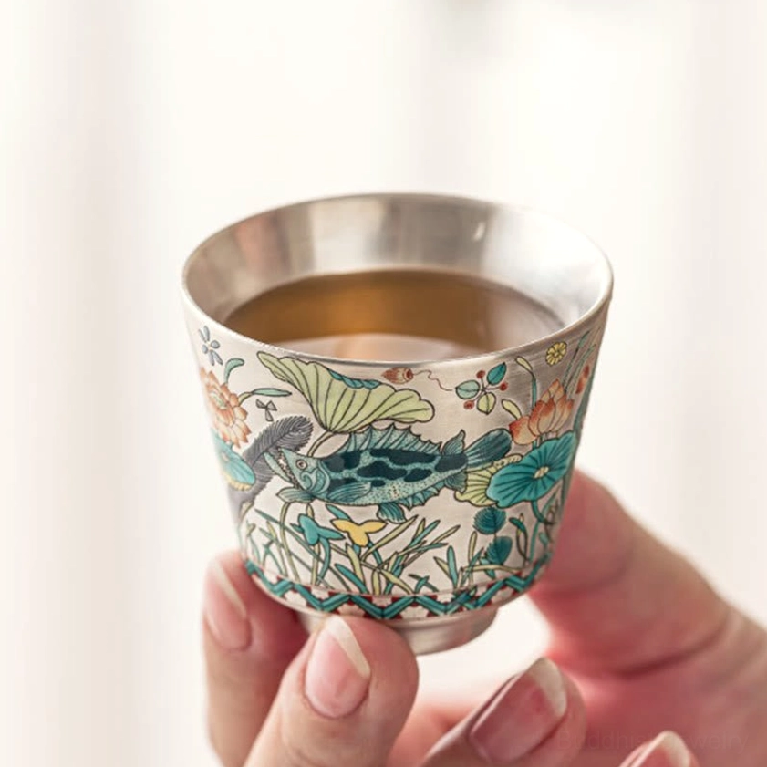 Premium handcrafted ceramic tea cup with silver-toned interior and fish-lotus design, angle view