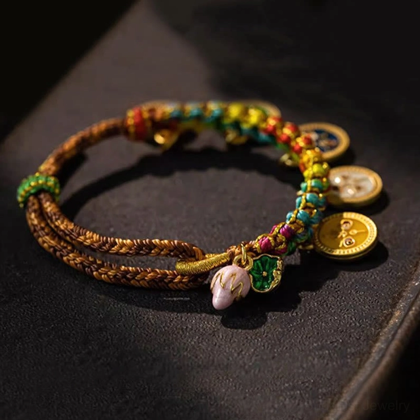 Close-up detail of Five Gods of Wealth bracelet on leather background, featuring multicolored braided cord with gold-toned enamel pendants representing prosperity deities
