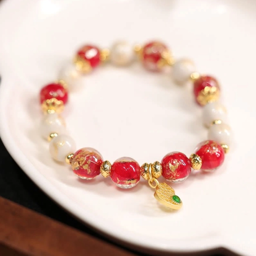 Top-down view of beaded bracelet with red and white beads, gold spacers, and dangling gourd charm on white ceramic plate
