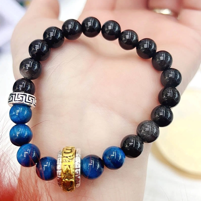Handmade obsidian tiger eye protection bracelet held in open palm showing bead detail and charm
