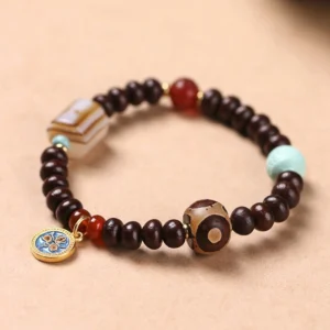 Purple bodhi seed dzi bead bracelet with yellow god of wealth charm displayed on wooden surface