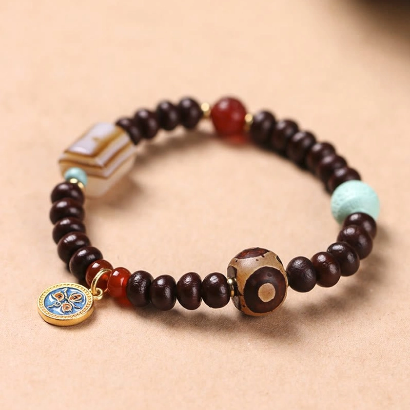 Purple bodhi seed dzi bead bracelet with yellow god of wealth charm displayed on wooden surface