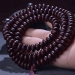 Purple Bodhi Seed 108 mala bracelet held in palm, showing deep reddish-brown beads with red tassel