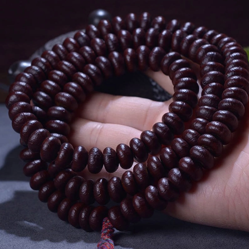 Purple Bodhi Seed 108 mala bracelet held in palm, showing deep reddish-brown beads with red tassel