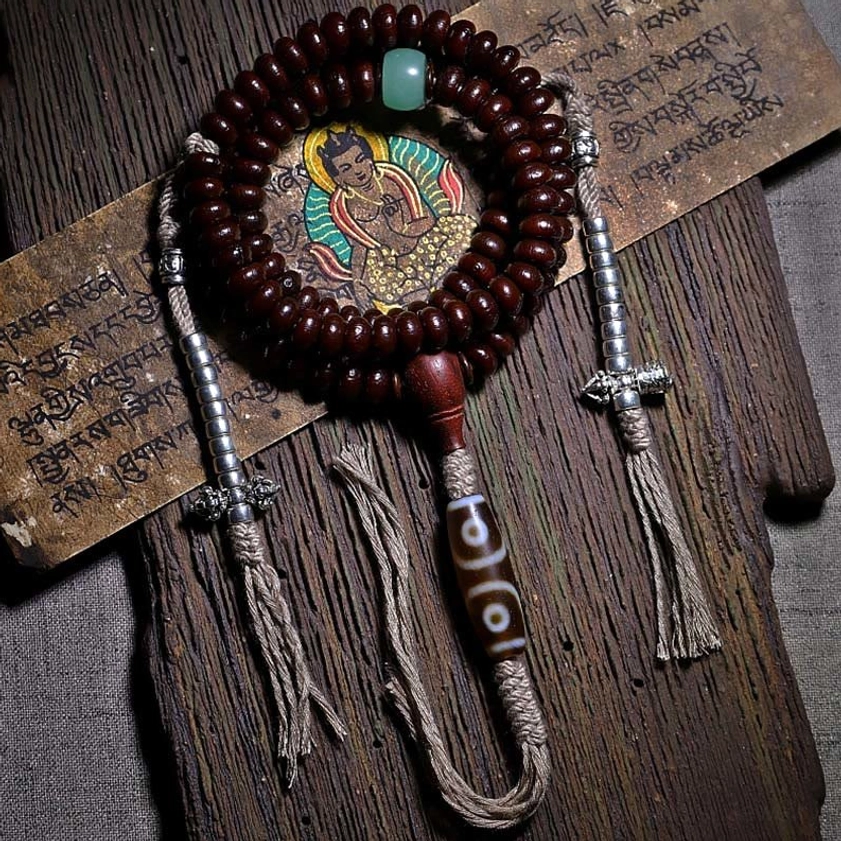 108 purple bodhi seed mala bracelet with three-eyed dzi bead and copper dorje displayed on wooden board with Buddhist sutra