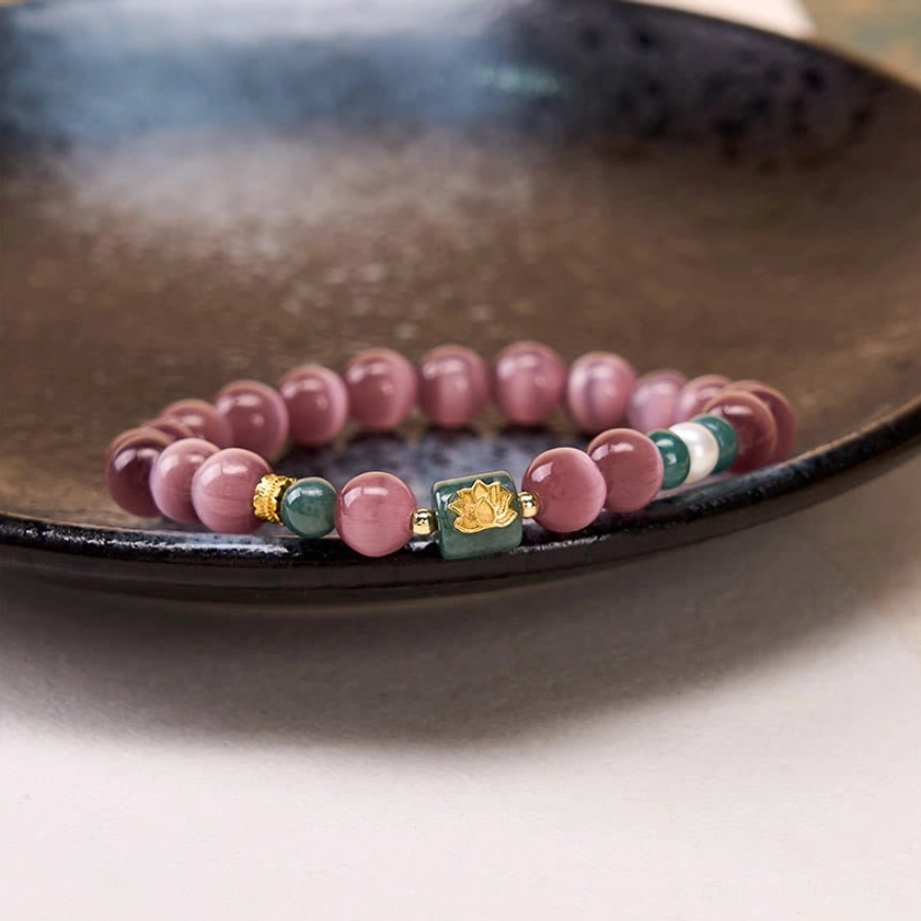 Purple cat's eye lotus beaded bracelet low angled view resting on dark brown ceramic plate with soft warm lighting