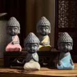 Four handcrafted purple clay Buddha statues with colorful robes on wooden surface, meditation and mindfulness desk decorations