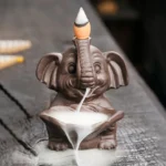 Purple clay elephant backflow incense burner with flowing smoke cascade on wooden surface, front view