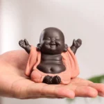 Handcrafted purple clay laughing Buddha statue held in palm, front three-quarter view showing smiling face and relaxed posture