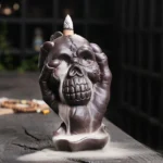 Purple clay skull backflow incense burner with ghost hand - front left three-quarter view showing flowing incense smoke from skull mouth