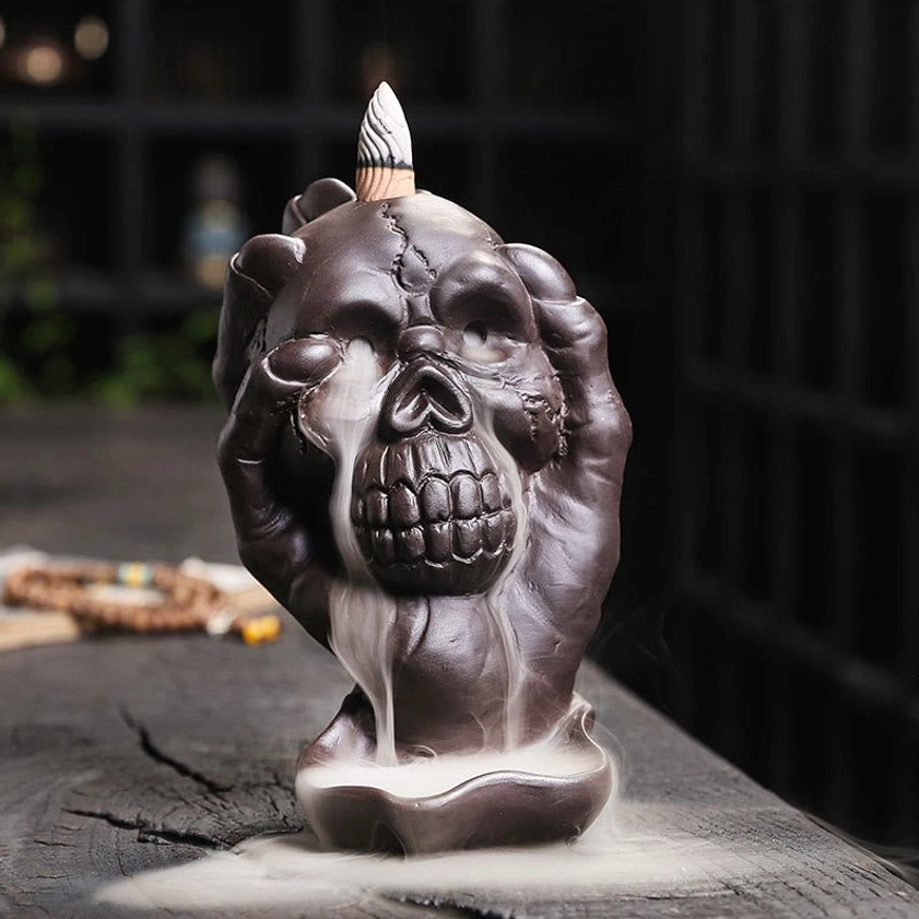 Purple clay skull backflow incense burner with ghost hand - front left three-quarter view showing flowing incense smoke from skull mouth