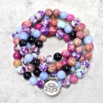 Purple Miano stone 108 bead lotus mala laid flat showing natural stone beads with silver lotus charm and metal spacers on gray surface