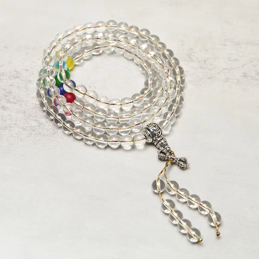 Buddhist prayer mala with clear quartz beads and multi-color chakra beads - side flat lay view showing coiled mala strands and silver metal tassel