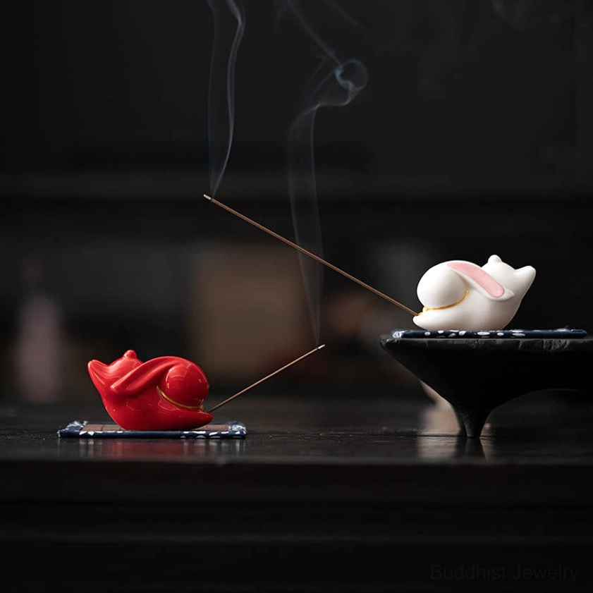 Red and white ceramic rabbit incense burners with burning incense and rising smoke in meditation display