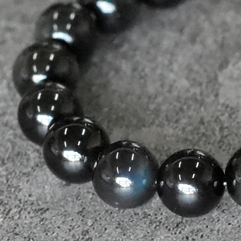 Macro close-up of polished rainbow obsidian beads with green-blue iridescent sheen and glossy spherical surface