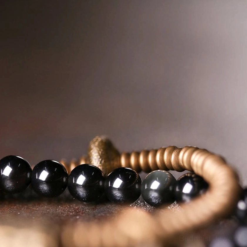 Close-up of rainbow obsidian beads with iridescent glow and bronze coil strands in natural light