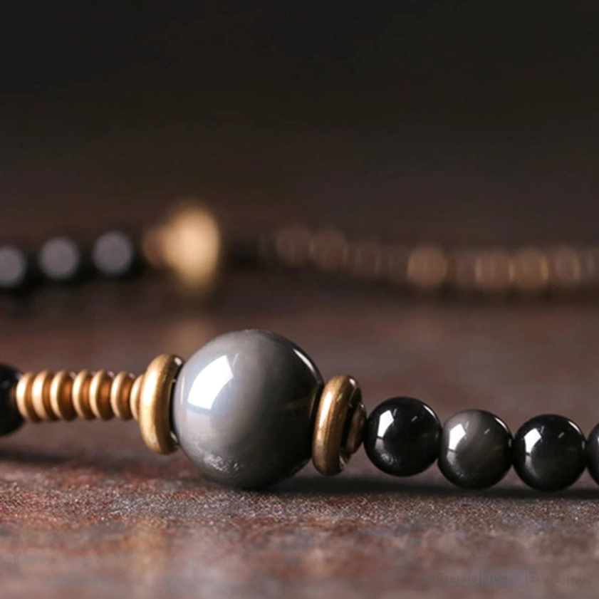 Macro close-up of rainbow obsidian Buddhist bracelet beads showing large gray obsidian bead bronze spacers and smooth black round beads in detail