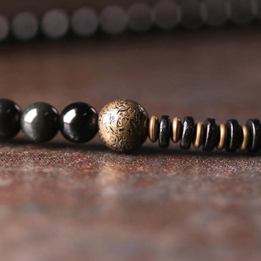 Macro flat lay of multilayer bracelet strand featuring carved bronze metal bead disc-shaped copper spacers and black obsidian beads