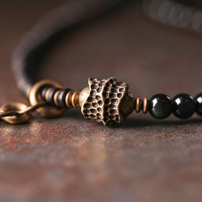 Detailed macro view of carved textured bronze metal bead matched with black round beads and copper spacers on multilayer Buddhist bracelet