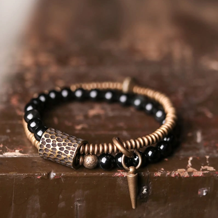 Handcrafted rainbow obsidian bracelet detail showing hammered bronze tube bead, coil beads and spike pendant on wooden surface
