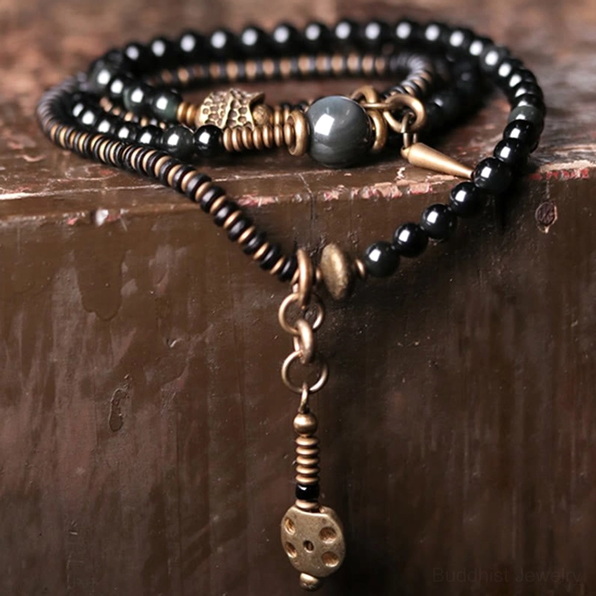 Ebony wood and rainbow obsidian Buddhist protection bracelet shown at eye level on dark wooden table with gray obsidian bead and metal dice pendant