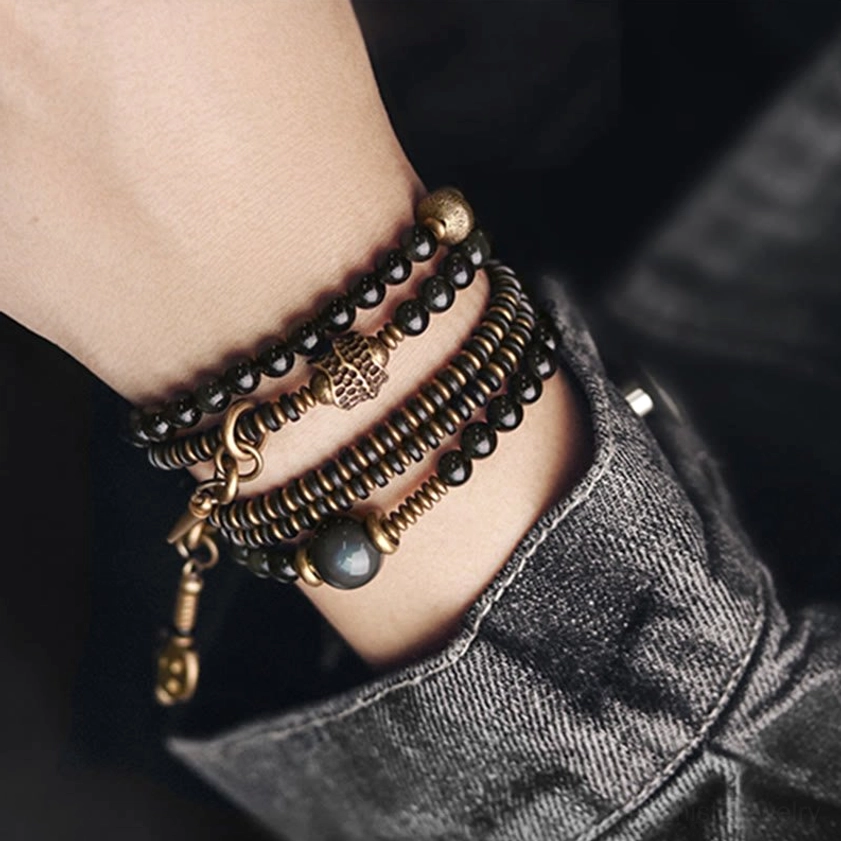 Rainbow Obsidian Buddhist bracelet with copper hardware and tassel pendants shown in lifestyle flat lay arrangement