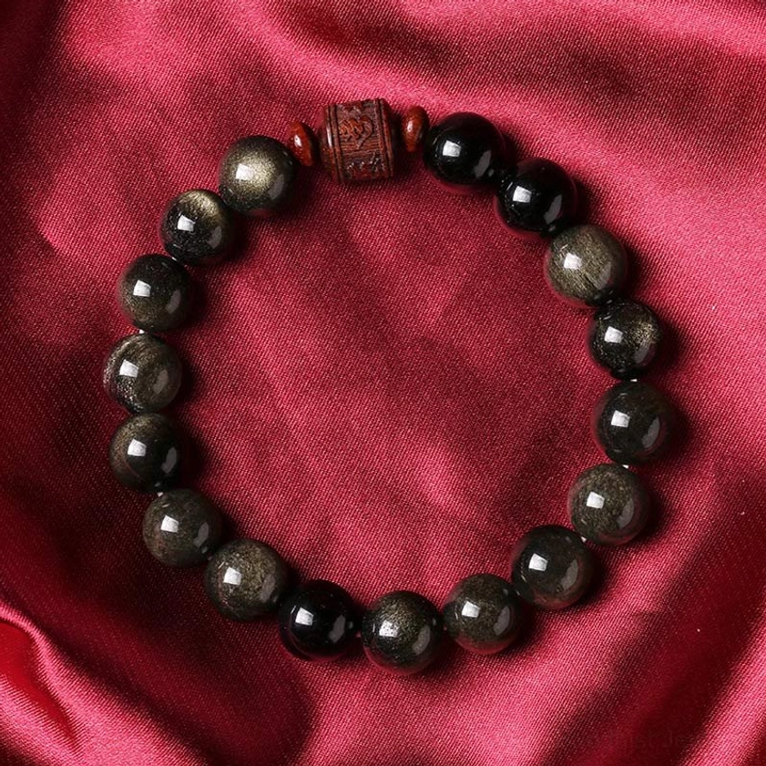 Rainbow obsidian Buddhist bracelet on red satin fabric, displaying deep black beads with golden lustrous finish and spiritual engravings