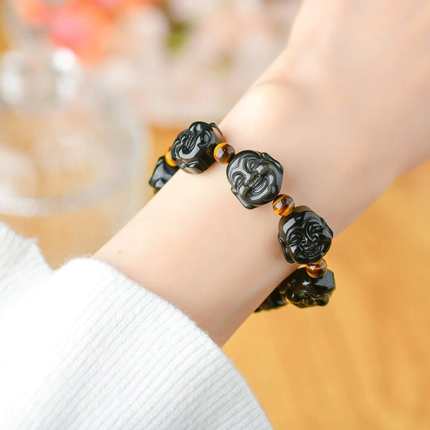 Rainbow obsidian Buddha bracelet worn on wrist with blurred floral background, demonstrating comfortable everyday wear fit