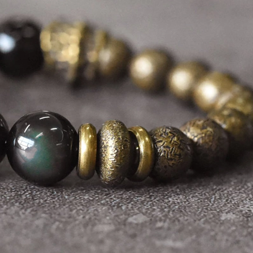 Side close-up of polished rainbow obsidian and bronze metal bracelet showing clear iridescent sheen on dark background