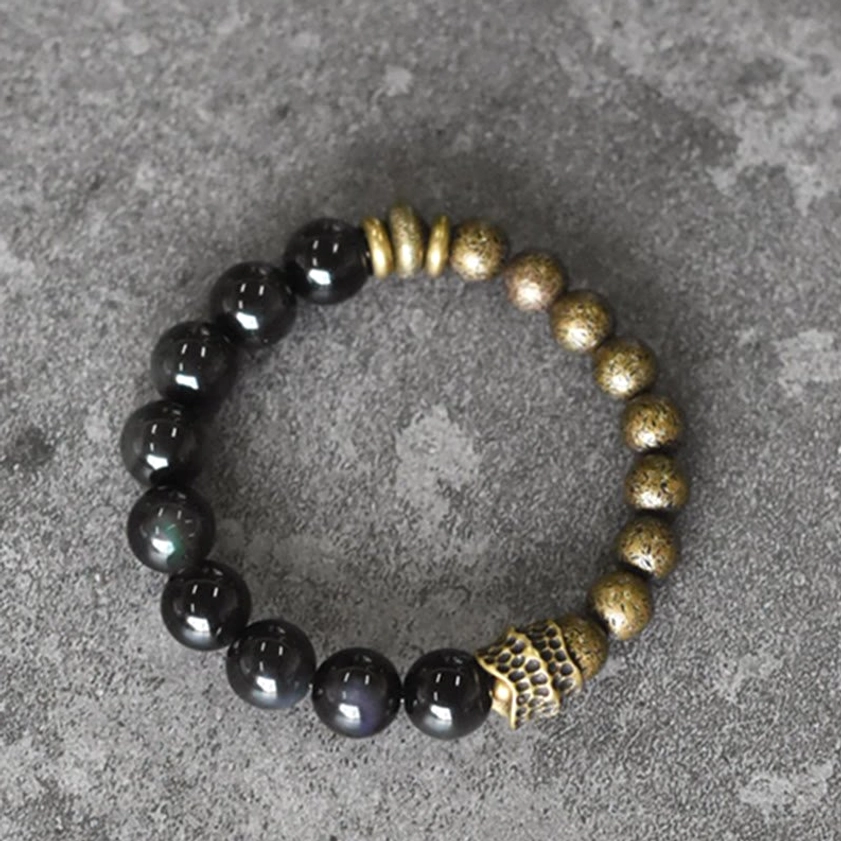 Full circular overhead view of obsidian copper bracelet with flat metal disc spacers on dark gray concrete surface
