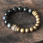 Rainbow obsidian and antique copper beaded bracelet with carved metal spacers, oblique overhead view on wood surface