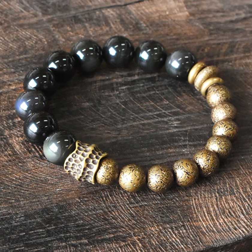 Rainbow obsidian and antique copper beaded bracelet with carved metal spacers, oblique overhead view on wood surface