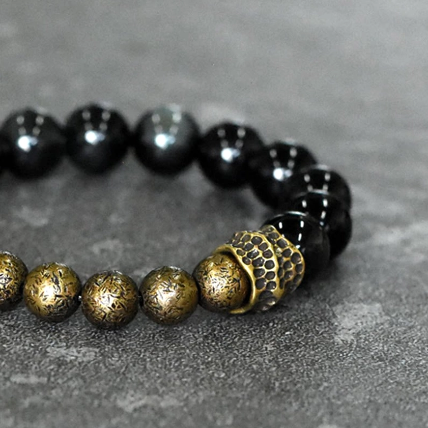 High-angle overhead view of rainbow obsidian copper bracelet with textured bronze bead spacers on light gray concrete