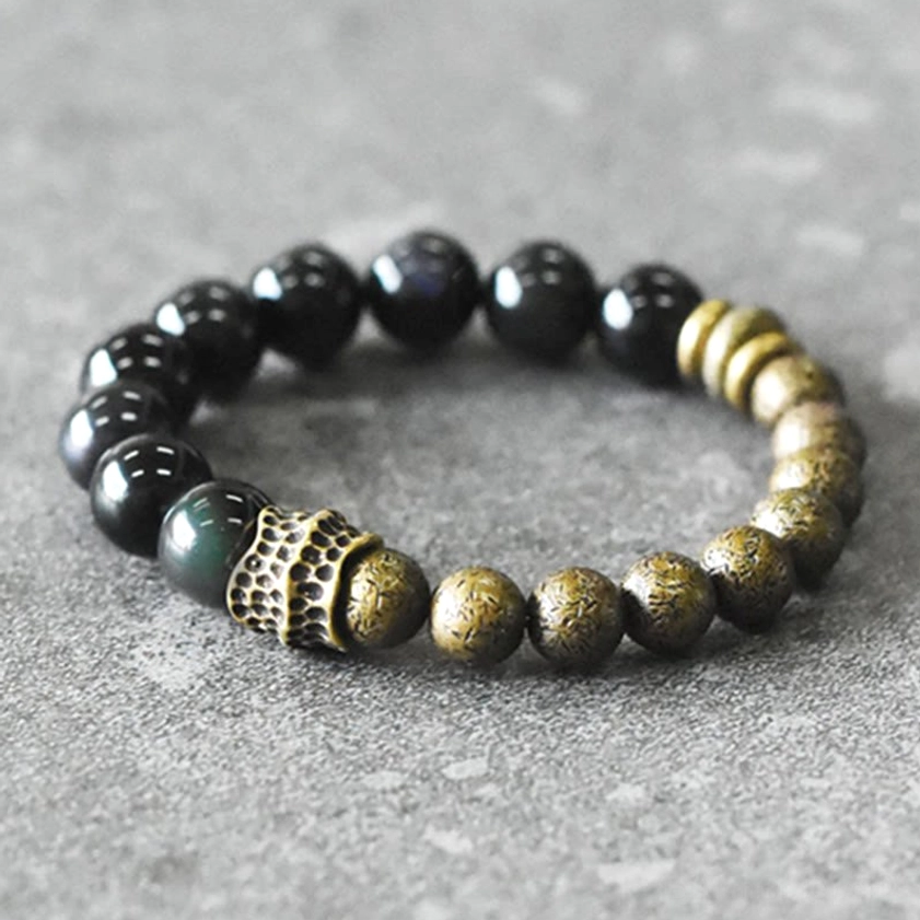Top-down overhead view of rainbow obsidian copper healing bracelet on light gray concrete background showing polished beads