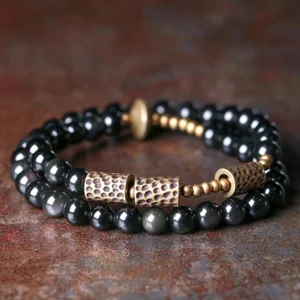 Rainbow obsidian double wrap bracelet with hammered copper accents, flat lay top view showing black glossy beads and bronze metal details on rustic tabletop