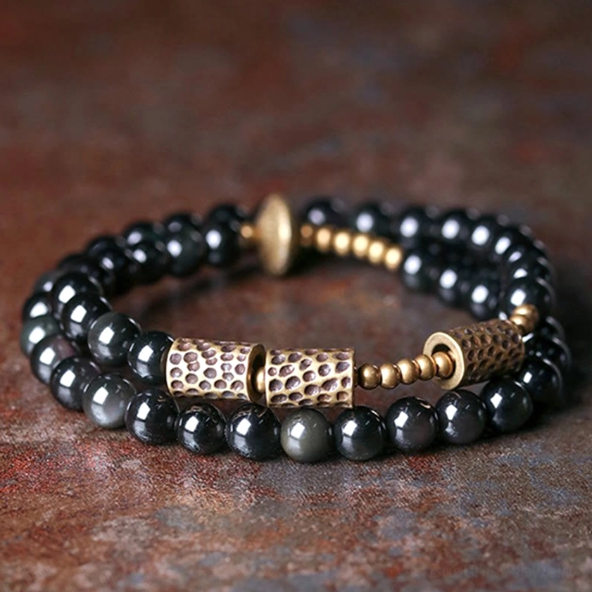 Rainbow obsidian double wrap bracelet with hammered copper accents, flat lay top view showing black glossy beads and bronze metal details on rustic tabletop