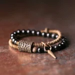 Rainbow obsidian double layer bracelet with copper hardware and spike charm, flat lay view showcasing antique bronze accents