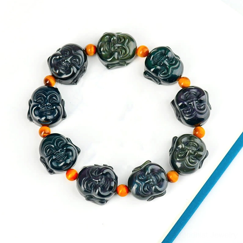 Rainbow obsidian laughing Buddha bracelet displayed on hardcover book, alternating carved Buddha heads with orange spacer beads