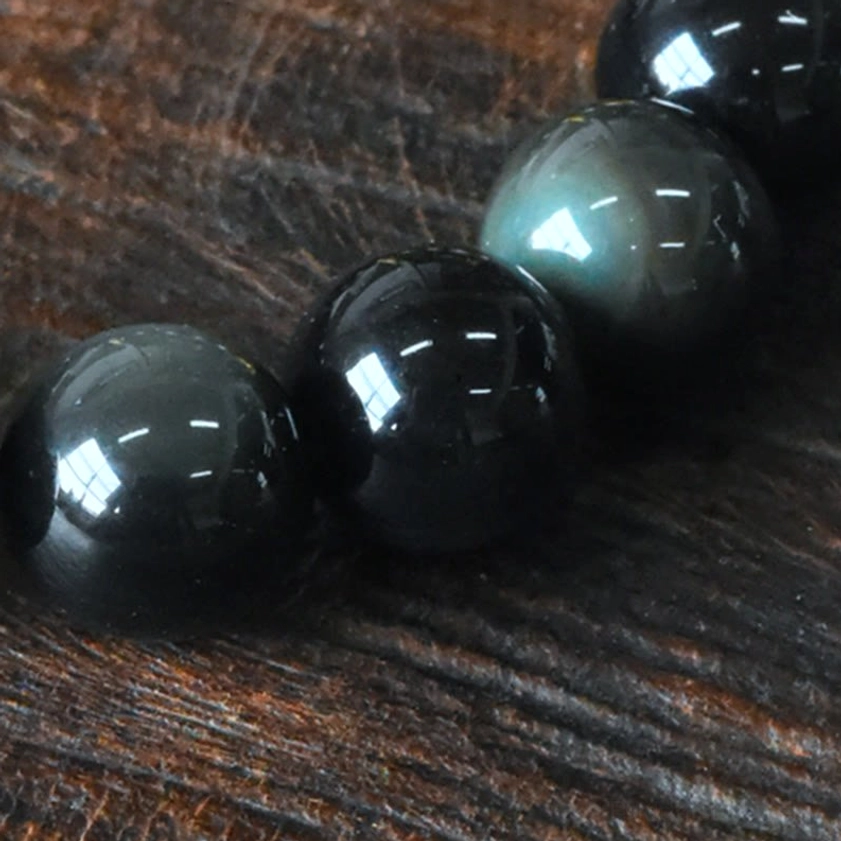 Overhead close-up of loose polished rainbow obsidian beads with rainbow iridescent finish on reflective surface