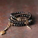 Rainbow Obsidian Ebony Wood Copper multilayer Buddhist bracelet set displayed overhead on vintage desktop with bronze hardware and tassel pendants